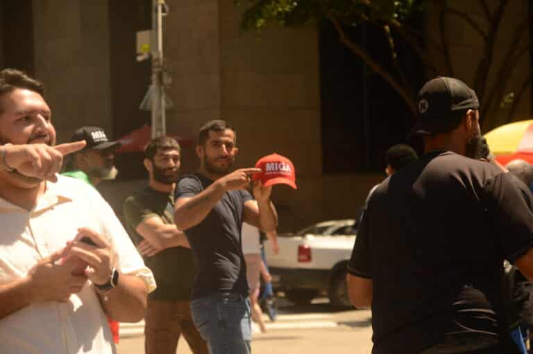 Manifestante iraniano aponta para boné MIGA enquanto vira o corpo e o boné para a câmera