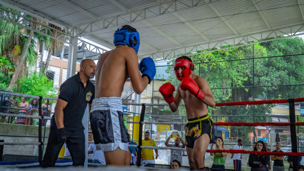 Dois lutadores num ringue com cena urbana de favela de fundo