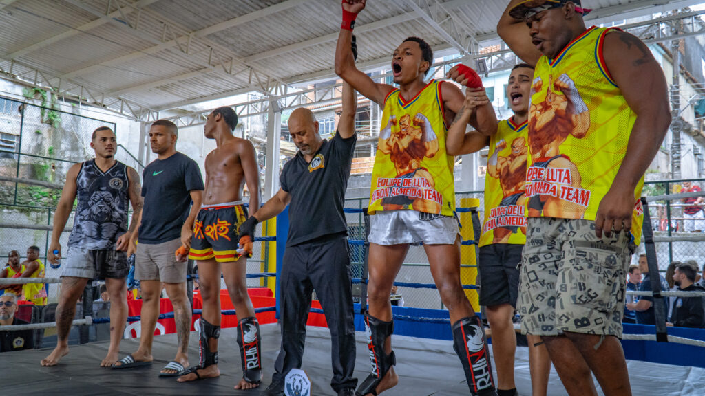 Árbitro declarando vencedor com a equipe dos lutadores presente no ringue